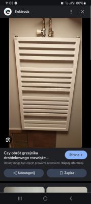 Nowo zamontowany biały grzejnik rurowy w łazience, widoczne przyłącza na górze.