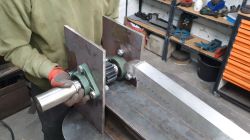 Gloved person holds a steel shaft with bearings and a gear next to a rack gear in a workshop