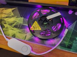 LED Spool with Control Button A spool of LED strip with purple LEDs on, lying on a desk with a control button on the cable.