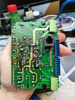 Spód płytki PCB z przypalonym obszarem i poprawianymi lutami, trzymana w dłoni