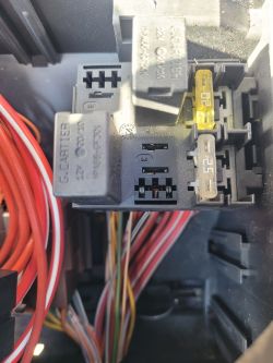 Zbliżenie na przekaźnik i gniazdo z kolorowymi kablami i żółtym bezpiecznikiem.