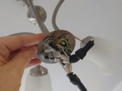 Ręka trzymająca podsufitkę żyrandola z widocznymi kablami elektrycznymi.