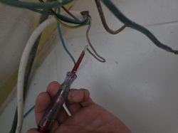 Próbnik napięcia dotyka luźnego, niepodłączonego kabla w ścianie