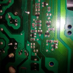 Zbliżenie na zieloną płytkę drukowaną z widocznymi elementami elektronicznymi i ścieżkami.