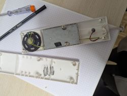 Plastic device casing opened to reveal speaker and internal electronics