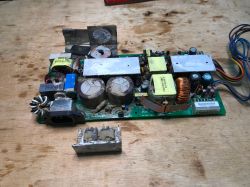 Wyjęty moduł zasilacza impulsowego z widocznymi śladami korozji i brudu na elementach elektronicznych.