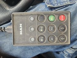 A MAN remote control with several buttons, resting on a person's jeans-clad lap.