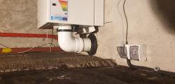 Biały element instalacji z kolanem rury przy szarej ścianie i gniazdku elektrycznym