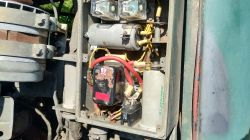 Otwarta skrzynka z instalacją elektryczną pojazdu: przekaźniki, cylindryczny element i grube czerwone przewody