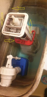 Wnętrze spłuczki WC z mechanizmem spustowym; żółte strzałki wskazują elementy do odkręcania