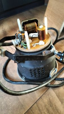 Lampa elektryczna z odsłoniętym mechanizmem i kablami na drewnianej podłodze.