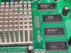 Fragment płyty głównej switcha z widocznym aluminiowym radiatorem oraz czterema kośćmi pamięci DRAM ESMT.