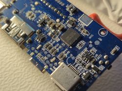 Zbliżenie na niebieską płytkę PCB z elementami elektronicznymi, w tym portem USB i mikroukładem.