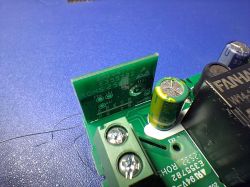 Close-up of a green PCB with a screw terminal, electrolytic capacitors, and a black component labeled FJAHH