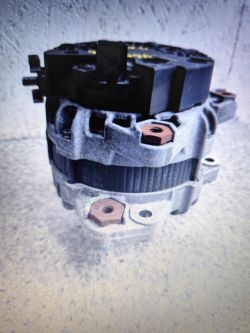 Alternator samochodowy z wyraźnie widocznymi zaciskami i korpusem aluminiowym