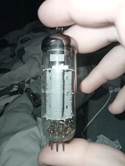Ręka trzyma lampę elektronową z ośmioma pinami na tle łóżka i innych lamp