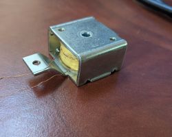 Mała cewka elektromagnesu w metalowej obudowie z dwoma cienkimi przewodami wychodzącymi z jednej strony.