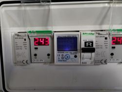 Panel elektryczny z wyświetlaczami napięcia pokazującymi 243 V i miernikiem energii.