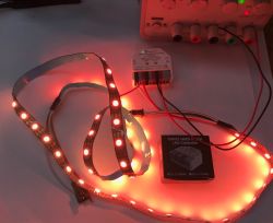 Red-glowing LED strip connected to an ESP32 WLED controller on a workbench
