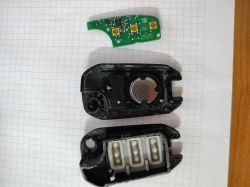 Rozłożony na części pilot do samochodu, w tym płytka obwodu i obudowa na kartce w kratkę.