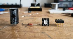 Cztery elementy elektroniczne na drewnianym stole: kondensator 2200 µF, dioda Zenera 5,1 V, moduł LED i podstawka DIP8