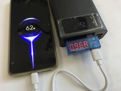 Phone charging from a power bank via a USB meter; phone shows 62%, meter reads 0.96 A.