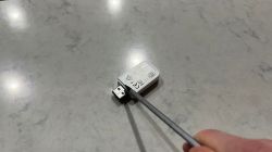 Micro USB Adapter Held by Screwdriver A small electronic adapter with a micro USB plug held by a screwdriver on a gray surface.
