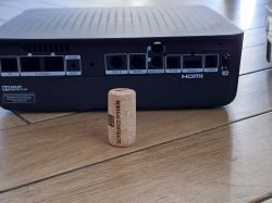 Tył czarnego dekodera z opisanymi portami i napisem HDMI; przed nim stoi korek od wina.