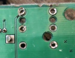Zbliżenie płytki PCB z przelotkami i przerwaną ścieżką w lewym górnym obszarze