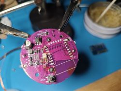 Printed circuit board held in a clamp against a blue workbench background.