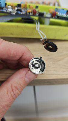 Zbliżenie na potencjometr obrotowy trzymany w dłoni, z płytką elektroniki w tle