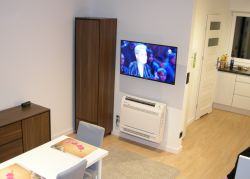 Pokój dzienny z zamontowanym telewizorem i klimatyzatorem na ścianie.