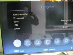 Widoczne menu na ekranie telewizora z refleksją osoby robiącej zdjęcie.