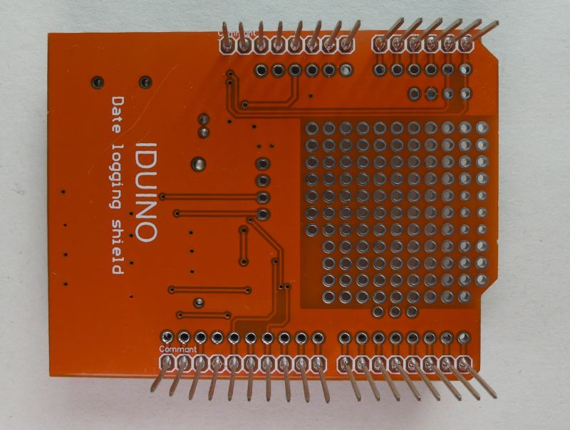 Spód pomarańczowej płytki PCB IDUINO, z pinami goldpin i polem otworów lutowniczych
