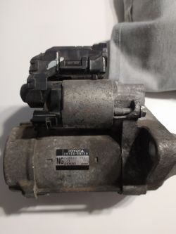 Rozrusznik samochodowy Denso 12V z numerem Toyota 28100-0N110 na stole.