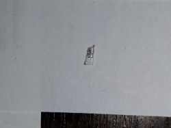 Ułamany przezroczysty narożnik matrycy leżący na białej kartce papieru.