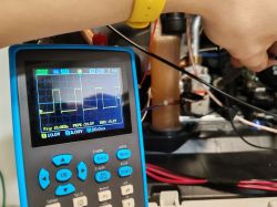 Digital oscilloscope showing PWM signal next to an open gas boiler casing