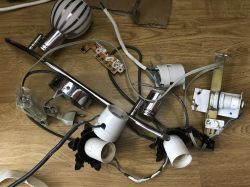 Dismantled lighting components, including lamp sockets, wires, and fixtures, lying on a wooden floor.