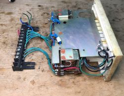 Opened relay device with metal cover, wires, and a screw terminal strip on a wooden workbench