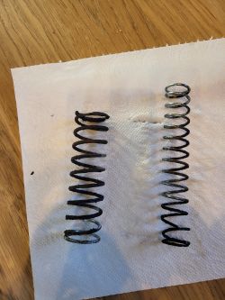 Dwie metalowe sprężyny o różnej długości leżące na papierowym ręczniku na drewnianym stole.