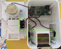 Interior view of a fish feeder with electronic components, highlighted switch, and infrared sensor.