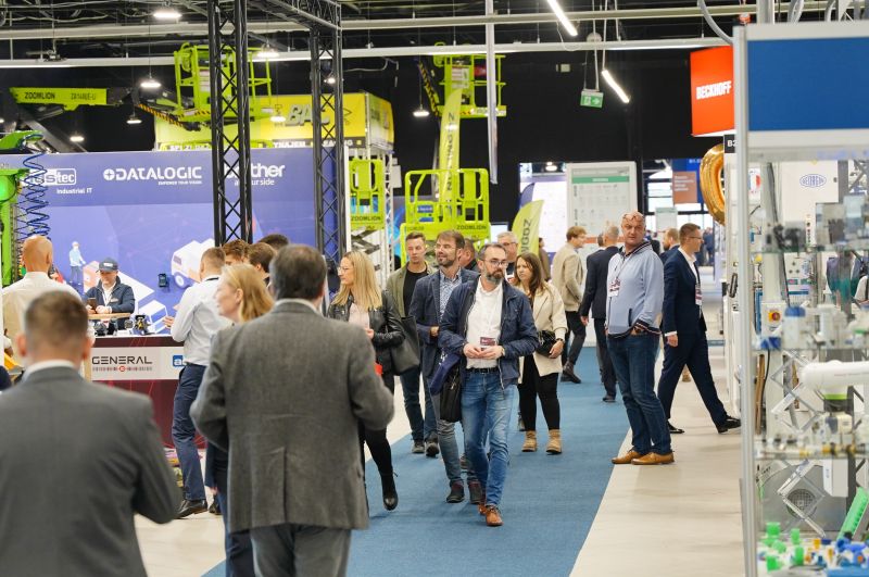 Crowd of people walking through an industrial trade fair hall with equipment displays.