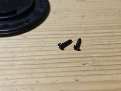 Black screws on wooden surface Two black screws on a wooden surface beside a black plastic component