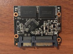 Zbliżenie na płytę drukowaną dysku SSD z widocznymi elementami elektronicznymi i złączem SATA.