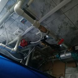 Instalacja hydrauliczna z rurami i pompą na tle ściany z płytek.
