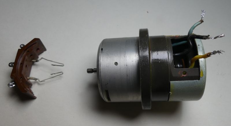 Das Bild zeigt Teile eines Selsyns, darunter einen Metallzylinder mit Drähten und ein Bauteil mit zwei Bürsten.
