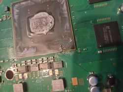 Zbliżenie na płytę główną PS3 Slim z widocznym procesorem i uszkodzeniami przy jego krawędzi.
