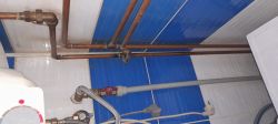 Instalacja hydrauliczna z rurami miedzianymi i niebiesko-białymi płytkami na ścianie.