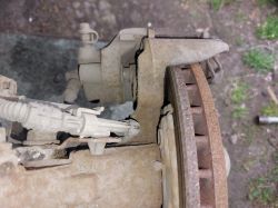 Zbliżenie na przedni zacisk hamulcowy i tarczę hamulcową samochodu, widoczne lekkie rdzawienie na krawędzi tarczy.