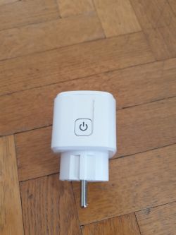 White smart plug with a power button on a wooden floor.